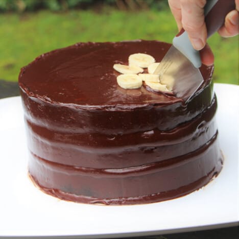 A three layer chocolate banana fosters cake being sliced to serve.
