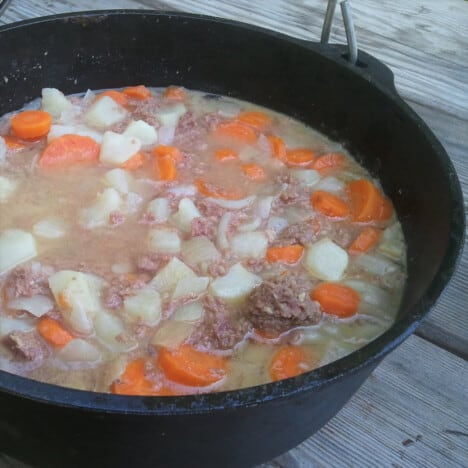 Close up of corned beef stew with chunks of carrot, potato, and onion in a Dutch oven.