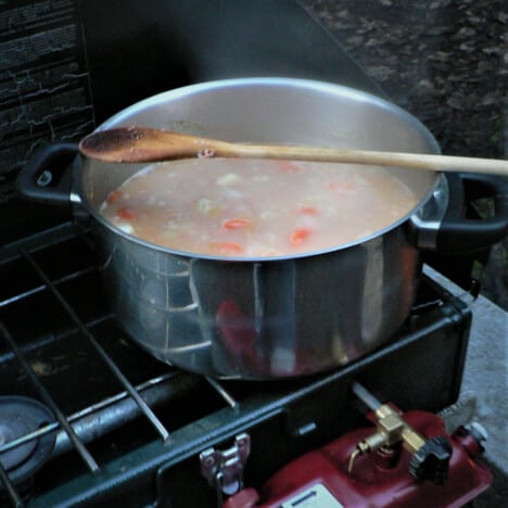 Steam rising from corned beef stew cooking in a stainless pot on a camp stove.