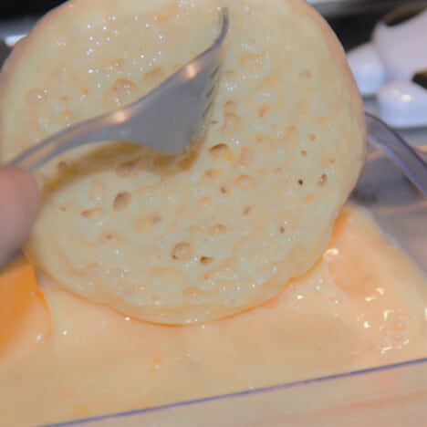 A crumpet round being removed from a dish of the egg mixture with a fork.