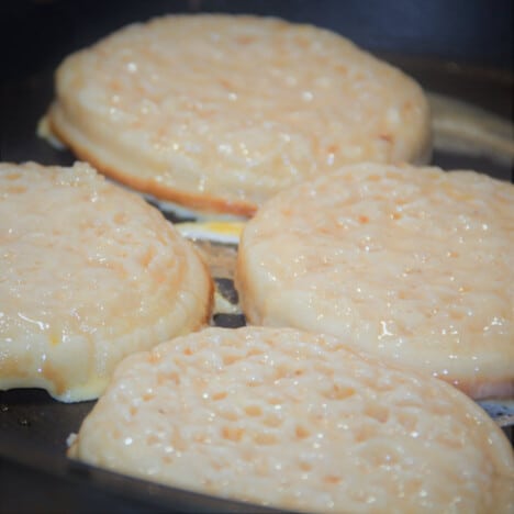 Several crumpets soaked in egg mixture frying in a skillet.