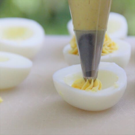 Close up of bag with metal tip beginning to pipe curried yolk mixture into a sliced egg half.