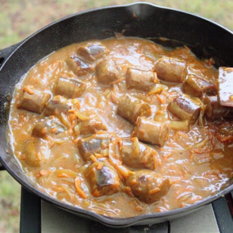 Sliced sausages, chopped onions, and grated carrots simmering in the curry sauce mixture in a cast iron frying pan.