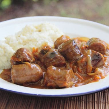 Completed curried sausages ready to serve on a white plate with a side of mashed potatoes.