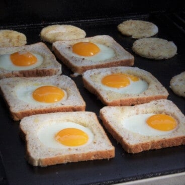 Six egg in breads in a row on a flat top griddle.