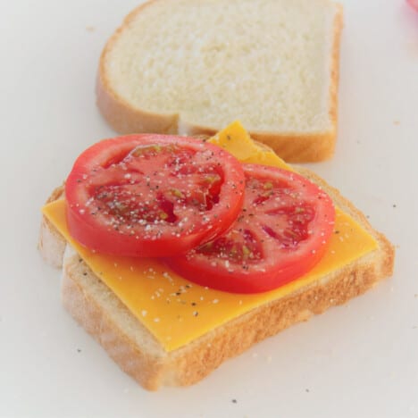 Two slices of bread with the closer having cheese, tomato, salt, and pepper on it.