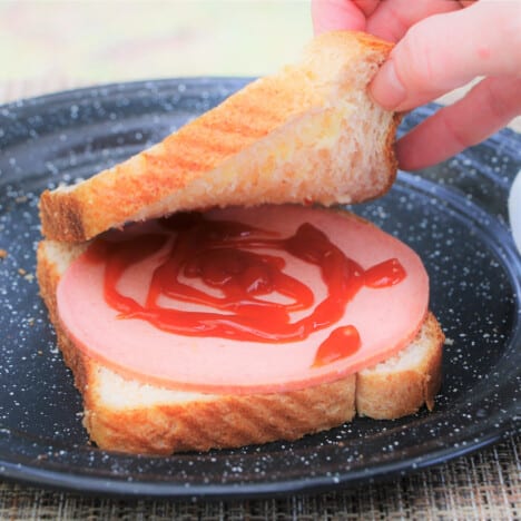The second slice of bread being placed on a heavy sauced fritz sandwich.