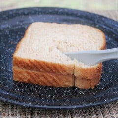 Close up of a fritz and sauce sandwich being cut in half on a black camp plate.