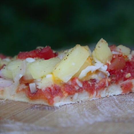 Close up of a slice of grilled ham and pineapple pizza ready to be eaten.