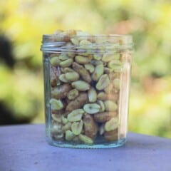 A clear glass jar full of nuts and bolts mix, peanuts and cereal coated in savory flavored oil and ready to eat.