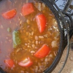 Overhead view of Omar’s Pinto Beans cooking in a Dutch oven with tomato slices and a jalapeno floating on top.