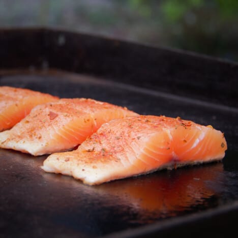 Three seasoned salmon filets cooking on a flat top grill.