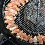 Seasoned chicken spare ribs in a curved row cooking via indirect heat along the outer edge of a grill over hot coals.