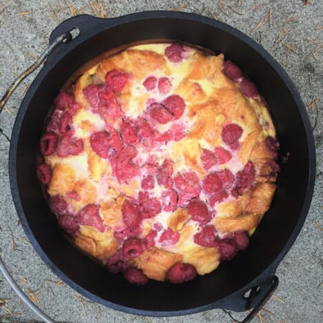 Overhead view of fully cooked, golden brown pudding studded with raspberries in a Dutch oven ready to serve.
