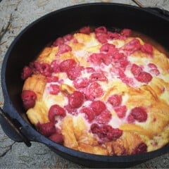 Fully cooked, golden brown pudding studded with raspberries in a Dutch oven ready to serve.