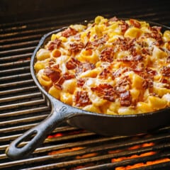 Smoked Mac ‘N’ Cheese cooking in a cast iron skillet on a grill with hot coals underneath.