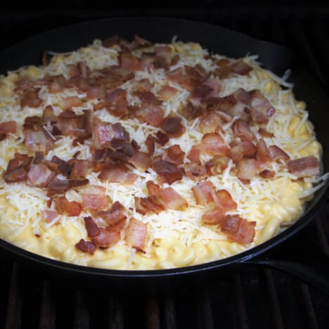 A mac and cheese with the topping of shredded cheese and crumpled bacon having just been added.