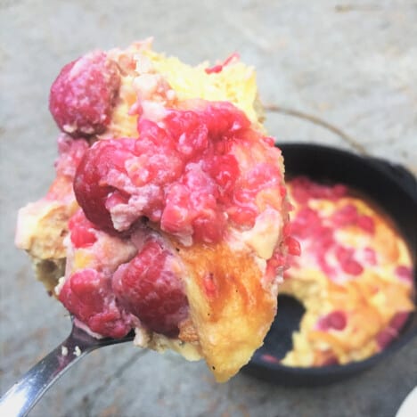 A single scoop of raspberry bread pudding is held above a Dutch oven.
