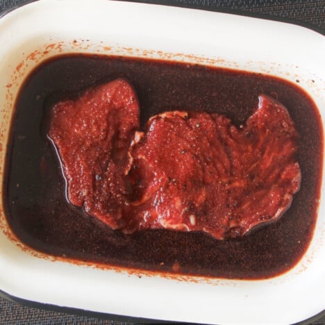 A rectangle dish with a steak marinating in it.