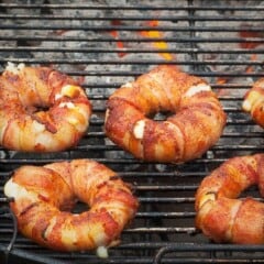 Bacon pineapple donuts cooking on a grill over charcoal.
