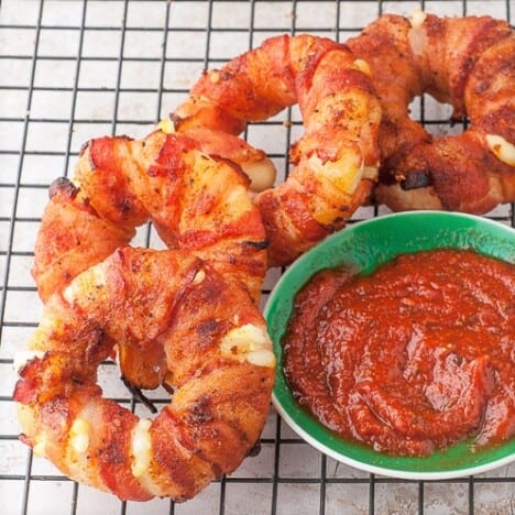A wire rack with bacon mozarella donuts and a green bowl of marinara dipping sauce.