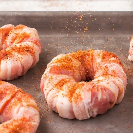 Rub being sprinkled over bacon wrapped onion mozarella donuts.