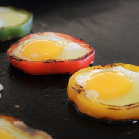 Eggs recently cracked into bell peppers cooking on a flat top grill.