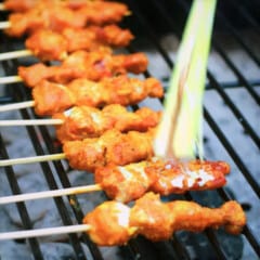 Chicken Satay on a grill being basted with coconut milk.