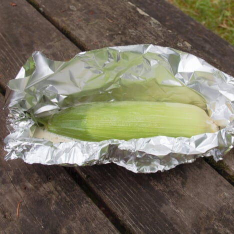 Raw corn being wrapped in foil to be cooked.