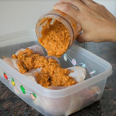 A paste being poured over chicken drumsticks in a plastic container.