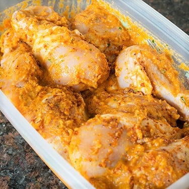 Chicken drumsticks in a plastic container surounded in a marinade.