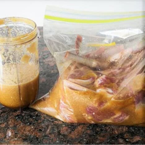A blender cup is sitting next to a plastic ziploack bag containing lamb ribs. Marinade is in both the cub and plastic bag.