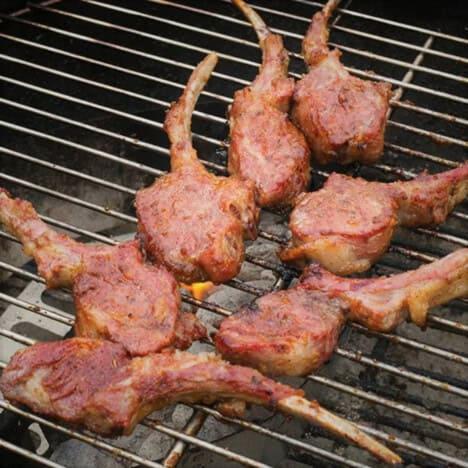 Looking down on a kettle grill with lamb chops cooking over charcoal.