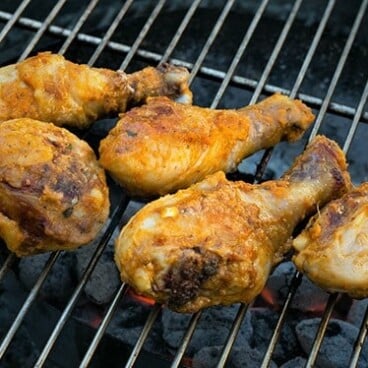 Seasoned chicken drumsticks grilling over charcoal.