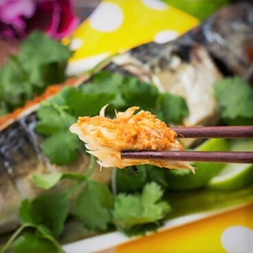 A piece of spicy grill mackerel being held with chopsticks.