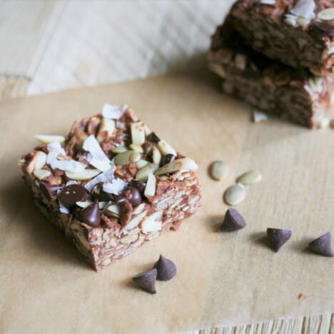 A single no bake energy bar, with chocolate chips and pepitas, sits on a piece of parchment paper.