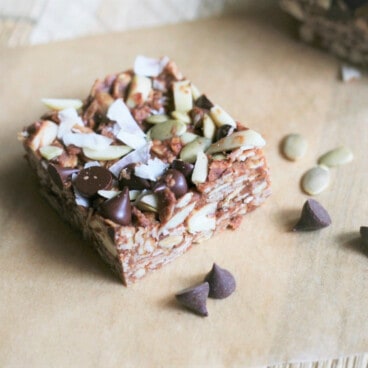 Looking down on a single no-bake energy bar on a piece of parchment paper, with chocolate chips and pepitas sprinkled around it.