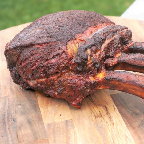 A smoked and grilled three bone standing rib roast sits on a chopping board awaiting slicing.