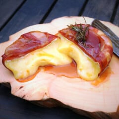 A prosciutto-wrapped Brie cut in half with the soft cheese inside oozing out onto the chopping board.