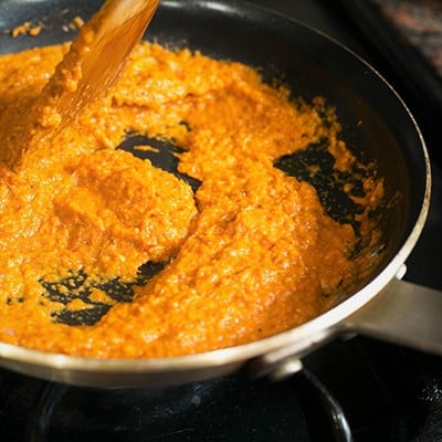 A fry pan with a wooden spoon stirring an orange spicy paste.