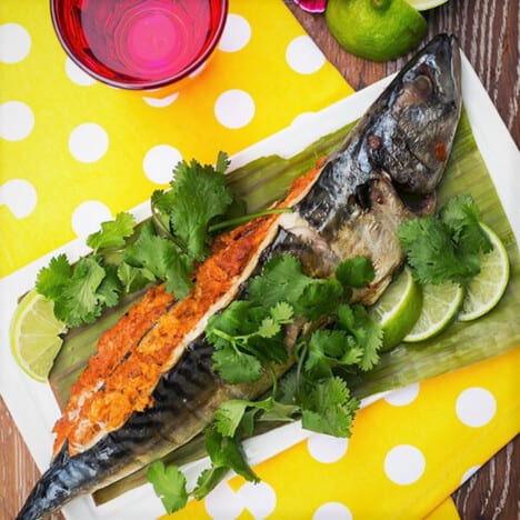 Whole cooked spicy mackerel served on a yellow placemat garnished with lime and cilantro.