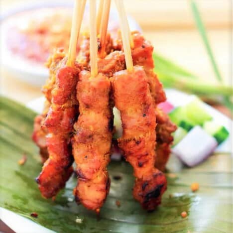 Chicken satay stick served standing up on a banana leaf.