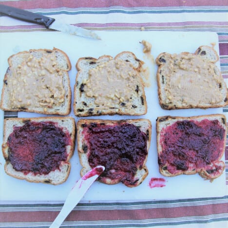Looking down on three slices of bread with peanut butter and three slices of bread with red jam.