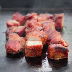 Cubes of boar belly on a flat top grill cooking.