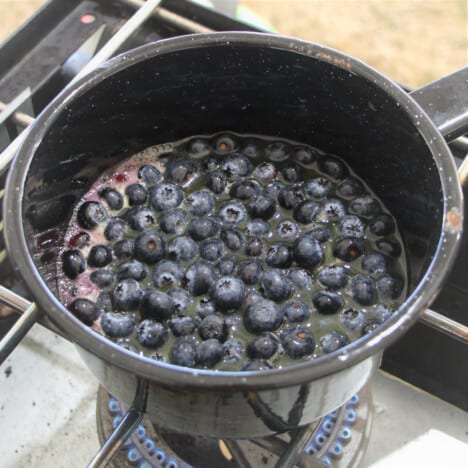 Blueberries simmering in an enamel camp saucepan cooking over a camp gas stove.