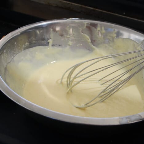 A whisk sitting in a stainless bowl along with a ricotta pancake batter.