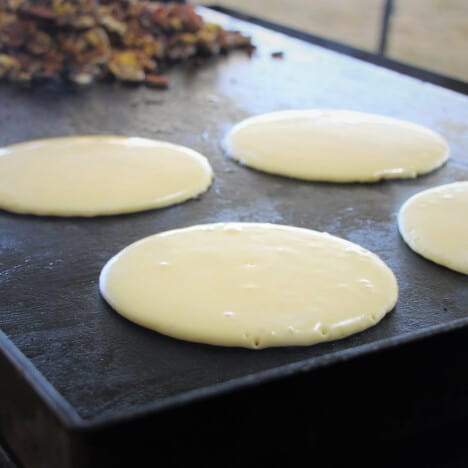 Four ricotta pancakes cooking on a flat top grill.