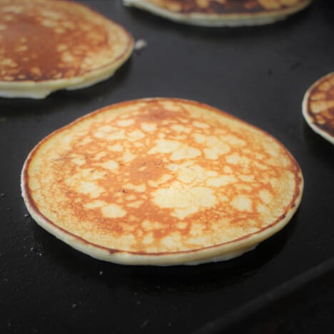 Close up of a golden brown ricotta pancake on a flat top grill.