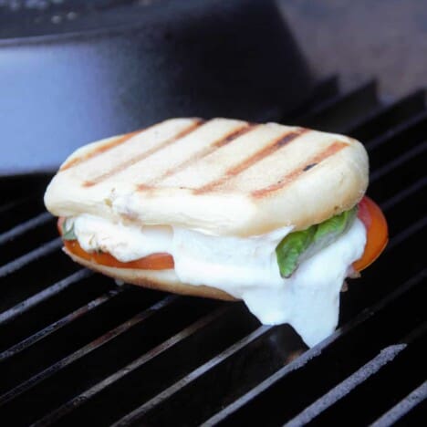 A grilled caprese panini on the grill, with the mozzarella cheese oozing out the sides.