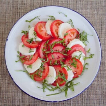 Looking down onto a pinwheel of sliced tomatoes and mozzarella sprinkled with basil.